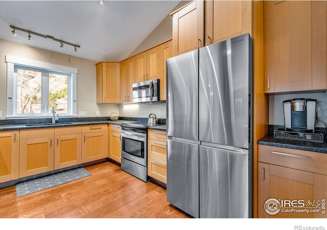 kitchen with dark countertops, light wood-type flooring, vaulted ceiling, stainless steel appliances, and a sink