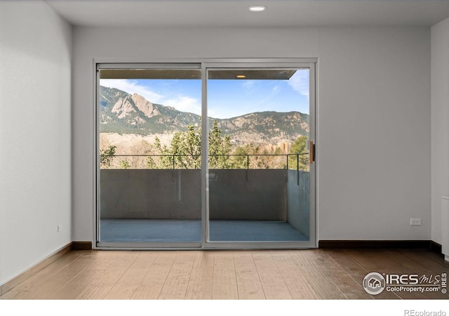 unfurnished room with wood finished floors, a mountain view, and baseboards