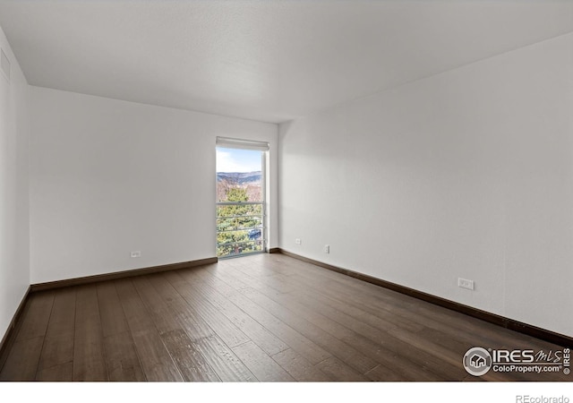 spare room with baseboards and dark wood finished floors