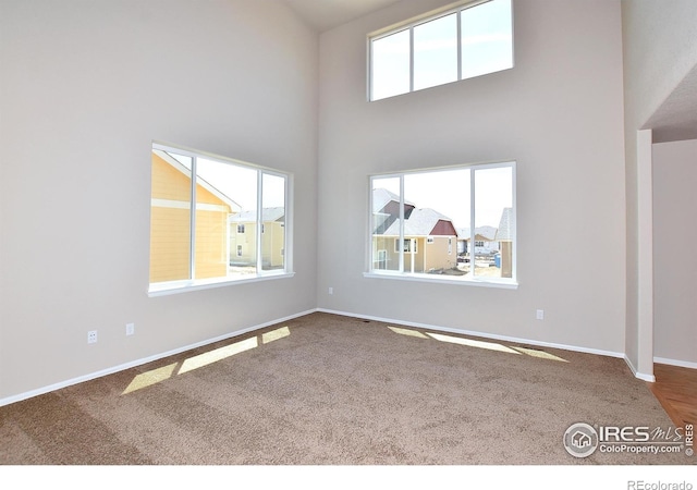 carpeted empty room with baseboards and a high ceiling