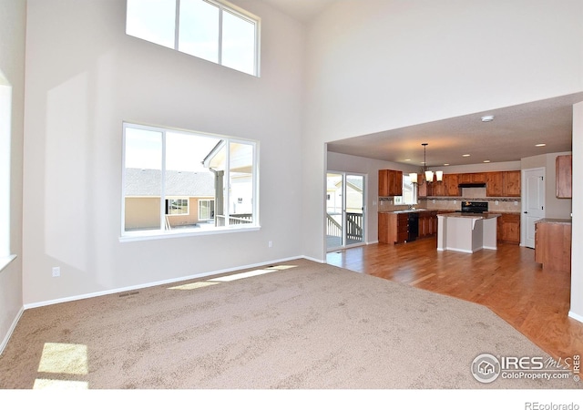 unfurnished living room featuring wood finished floors, baseboards, recessed lighting, a towering ceiling, and carpet flooring