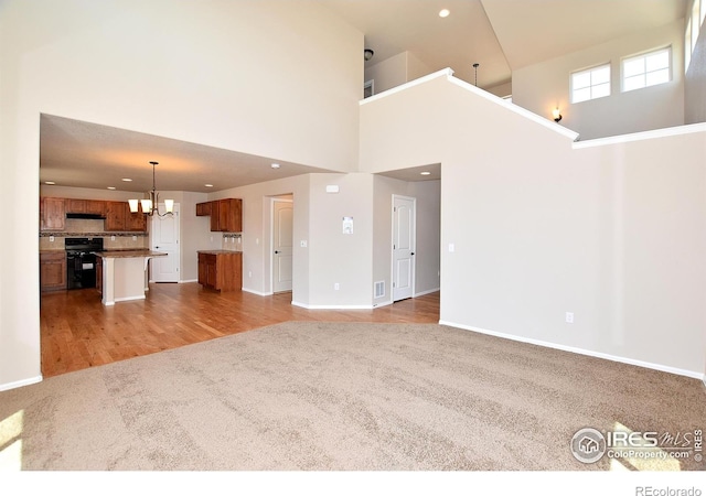 unfurnished living room with baseboards, carpet floors, an inviting chandelier, recessed lighting, and a towering ceiling