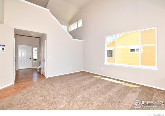 unfurnished living room featuring carpet flooring, wood finished floors, baseboards, and high vaulted ceiling