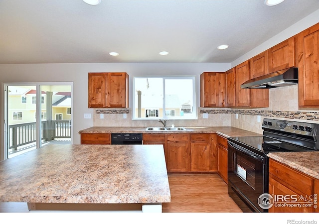 kitchen featuring under cabinet range hood, black appliances, brown cabinetry, and a sink