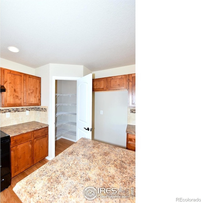 kitchen with light stone counters, backsplash, light wood-style floors, brown cabinetry, and range