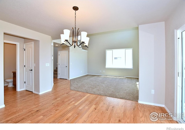 spare room with a chandelier, light wood-style flooring, and baseboards