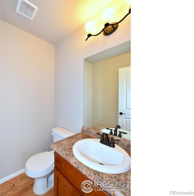 bathroom featuring visible vents, baseboards, toilet, wood finished floors, and vanity