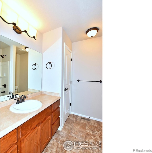 full bath featuring vanity, baseboards, stone finish floor, a shower, and toilet