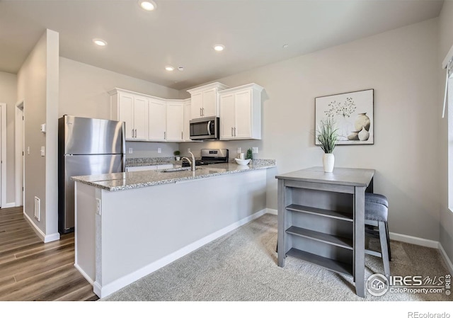 kitchen with light stone counters, a sink, white cabinetry, stainless steel appliances, and a peninsula