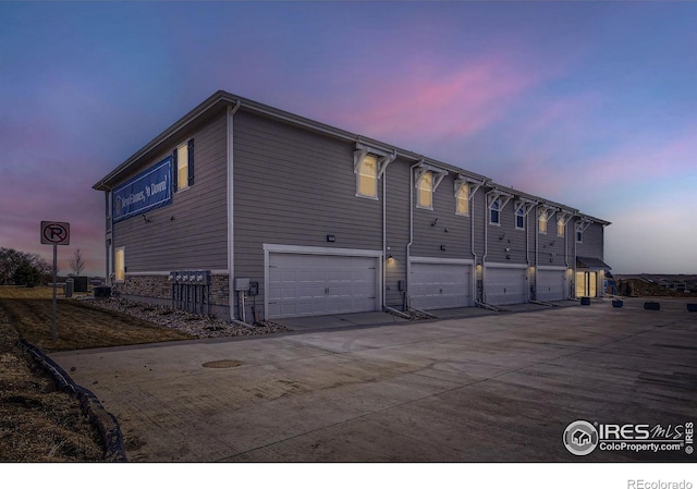 back of house at dusk with concrete driveway and an attached garage