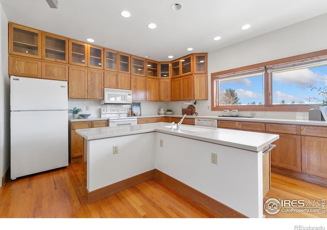 kitchen featuring brown cabinets, light wood finished floors, white appliances, light countertops, and glass insert cabinets