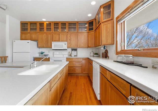 kitchen featuring backsplash, light countertops, brown cabinets, white appliances, and a sink