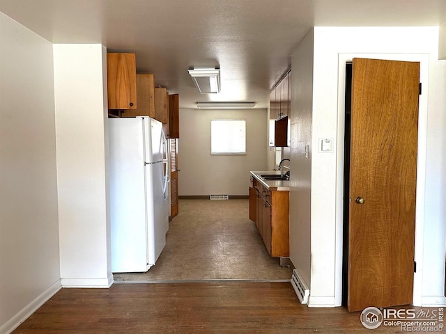 kitchen featuring wood finished floors, brown cabinetry, visible vents, freestanding refrigerator, and a sink