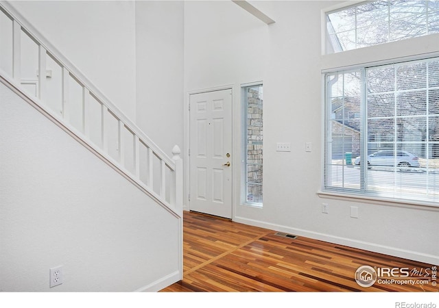 foyer entrance featuring stairway, visible vents, baseboards, a towering ceiling, and light wood-type flooring