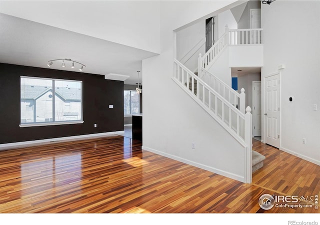 unfurnished living room with stairs, a high ceiling, wood finished floors, and baseboards