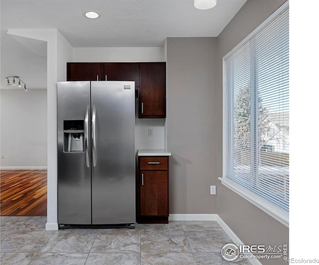 kitchen featuring a textured ceiling, stainless steel fridge, light countertops, baseboards, and dark brown cabinets