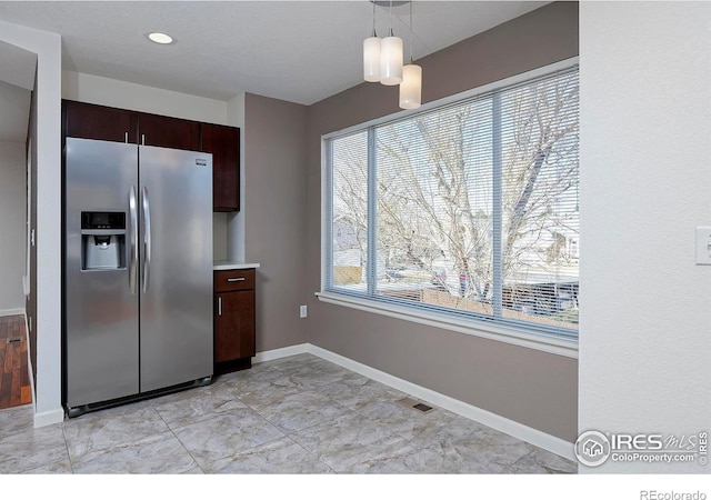 kitchen featuring dark brown cabinets, baseboards, stainless steel fridge with ice dispenser, pendant lighting, and light countertops