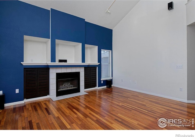 unfurnished living room with a tile fireplace, high vaulted ceiling, and wood finished floors