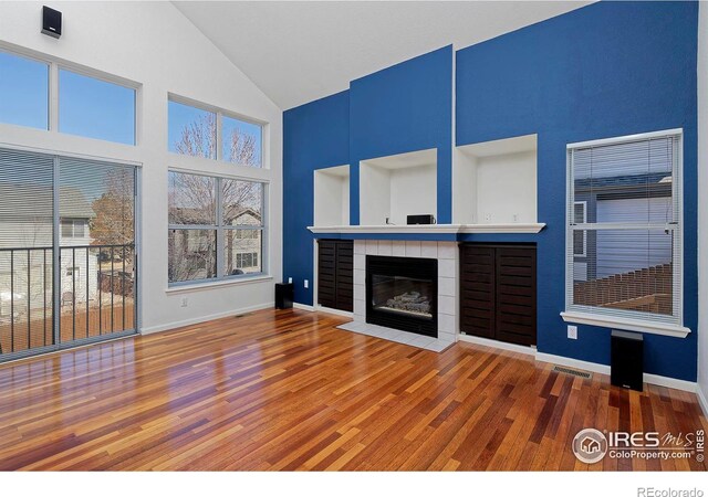 living area with visible vents, high vaulted ceiling, a tiled fireplace, wood finished floors, and baseboards