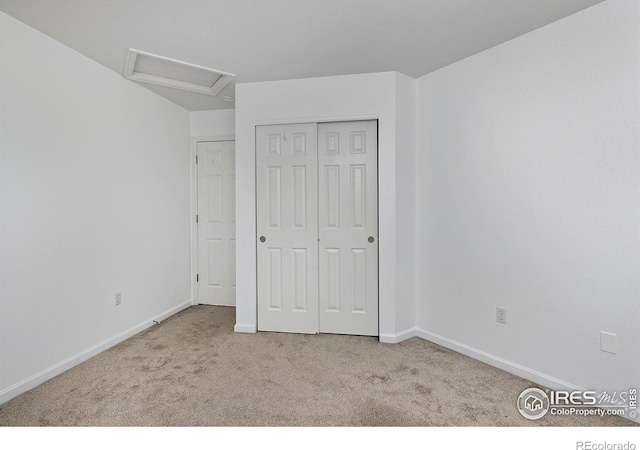 unfurnished bedroom with a closet, baseboards, attic access, and carpet flooring