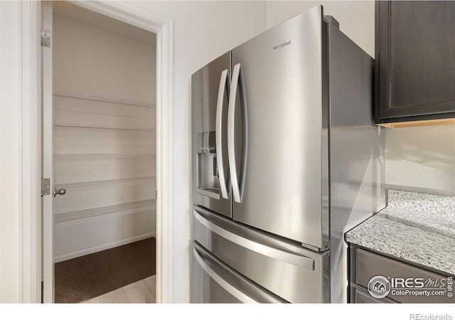 details with light stone countertops, dark brown cabinets, and stainless steel refrigerator with ice dispenser