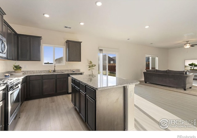 kitchen featuring light wood-style flooring, a ceiling fan, a sink, light stone counters, and appliances with stainless steel finishes