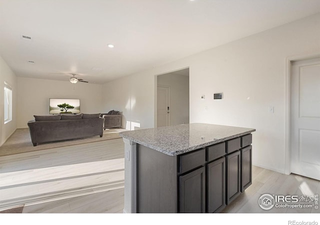 kitchen featuring light wood finished floors, visible vents, a center island, light stone counters, and a ceiling fan