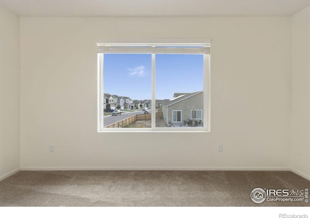 empty room with a residential view, baseboards, and carpet floors