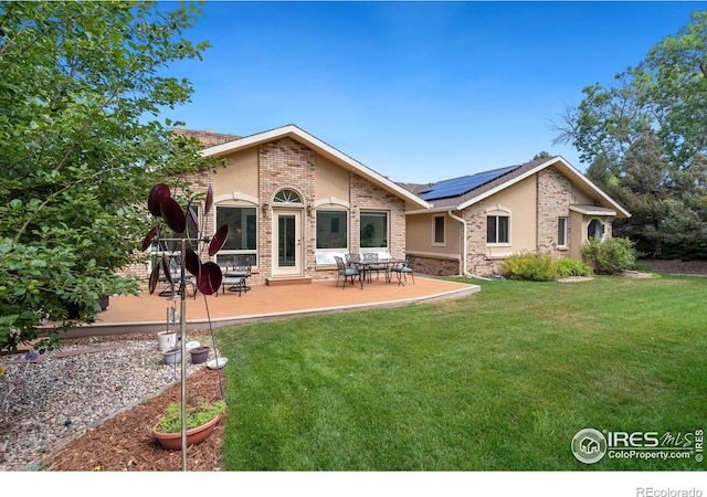 rear view of house with brick siding, solar panels, stucco siding, a yard, and a patio area