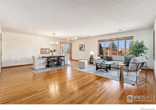 living area featuring a notable chandelier, a textured ceiling, light wood-type flooring, and baseboards