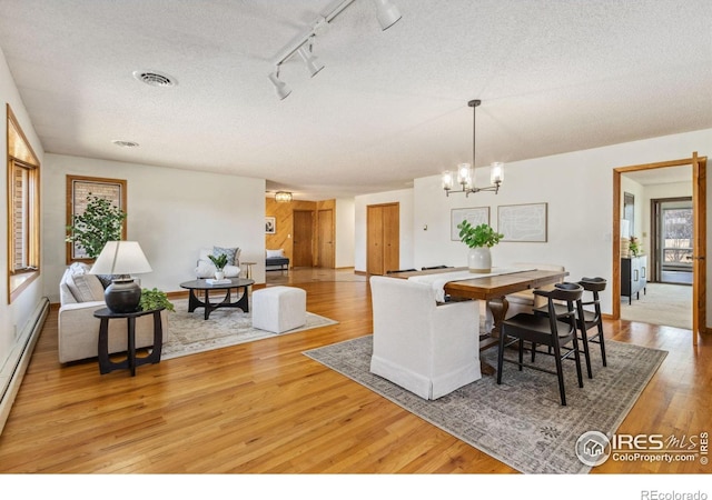 dining room featuring visible vents, light wood-style flooring, a textured ceiling, a notable chandelier, and baseboard heating