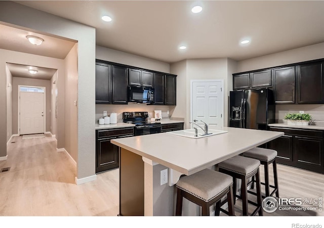 kitchen with a kitchen bar, black appliances, light wood-style flooring, and a sink