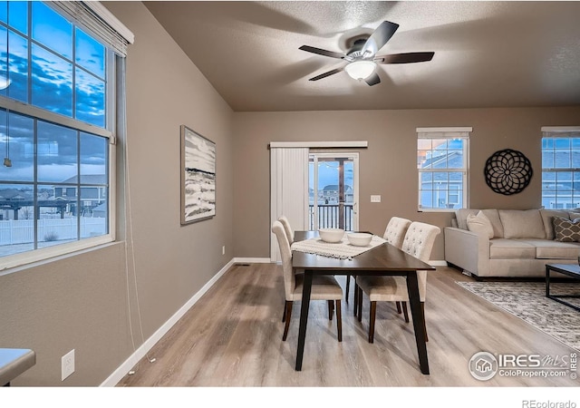 dining space featuring a textured ceiling, baseboards, light wood-type flooring, and ceiling fan