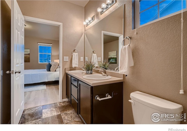 full bathroom featuring a sink, toilet, stone tile flooring, and double vanity