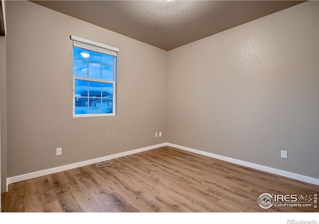 empty room featuring visible vents, a textured ceiling, baseboards, and wood finished floors