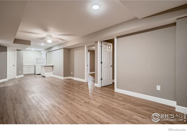 finished below grade area featuring light wood-style flooring, baseboards, and freestanding refrigerator