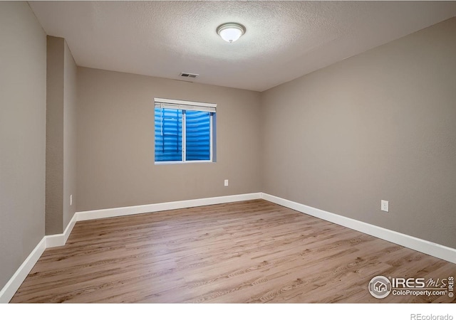 unfurnished room featuring baseboards, wood finished floors, visible vents, and a textured ceiling