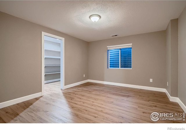 unfurnished room with visible vents, a textured ceiling, baseboards, and wood finished floors