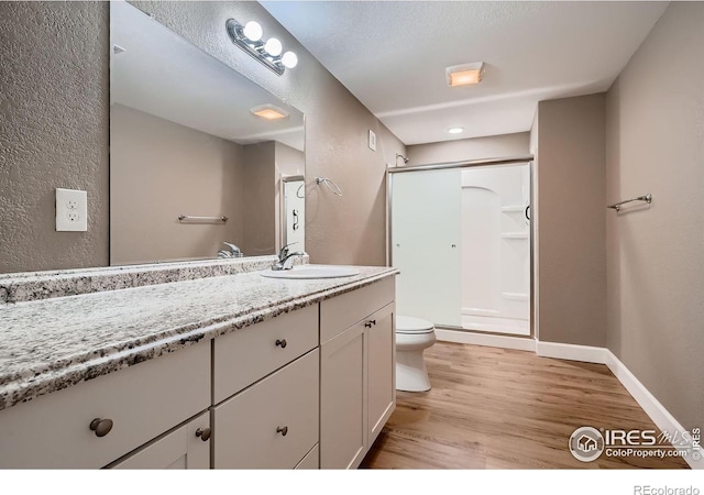 full bath featuring toilet, wood finished floors, a shower stall, baseboards, and vanity