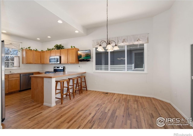 kitchen featuring light countertops, light wood-style flooring, appliances with stainless steel finishes, a kitchen breakfast bar, and a notable chandelier