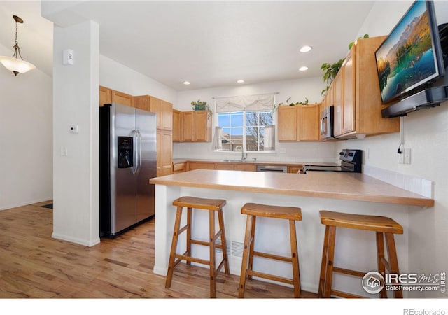 kitchen featuring a sink, light wood-style floors, appliances with stainless steel finishes, a peninsula, and light countertops