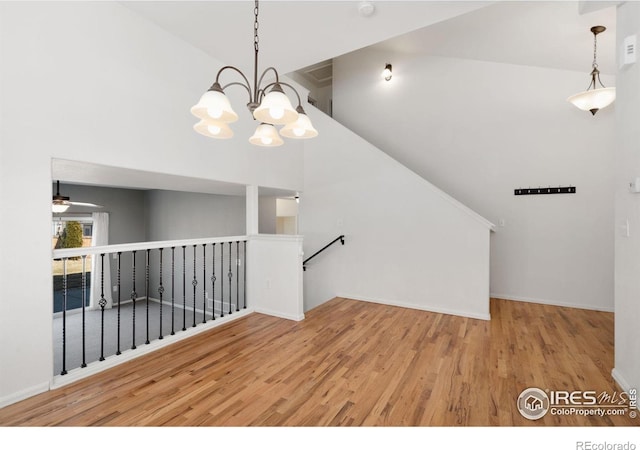 empty room featuring ceiling fan with notable chandelier, wood finished floors, and high vaulted ceiling