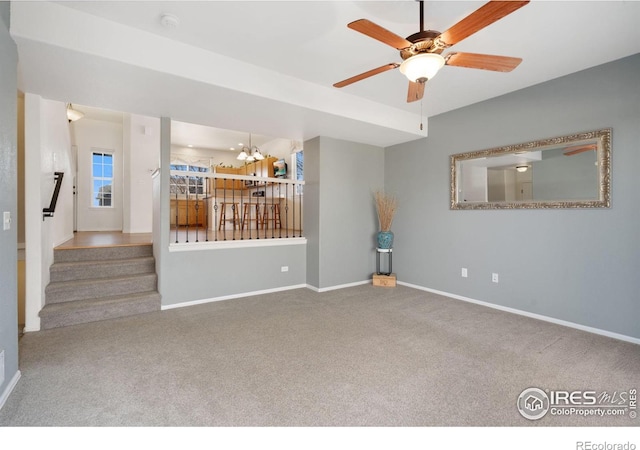 unfurnished living room featuring ceiling fan with notable chandelier, stairs, baseboards, and carpet floors