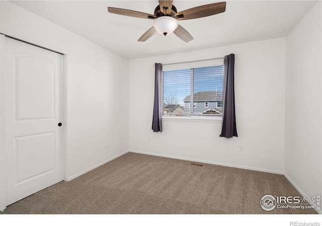 carpeted empty room with visible vents, baseboards, and ceiling fan