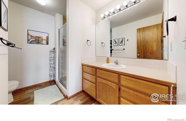 bathroom featuring wood finished floors, toilet, a stall shower, and vanity