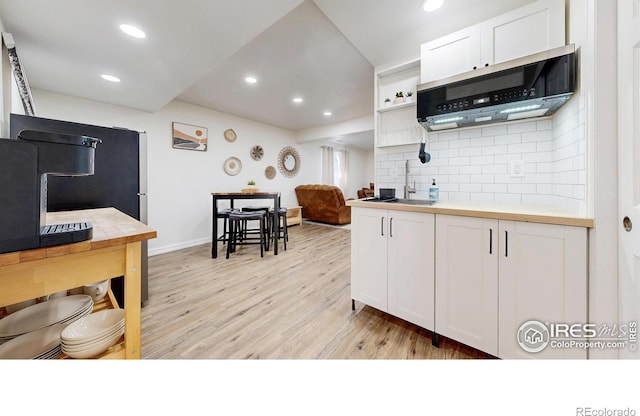 kitchen with recessed lighting, white cabinets, light wood-style floors, stainless steel microwave, and backsplash