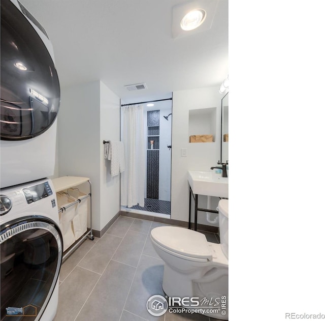 bathroom featuring tile patterned flooring, visible vents, toilet, a stall shower, and stacked washer / drying machine