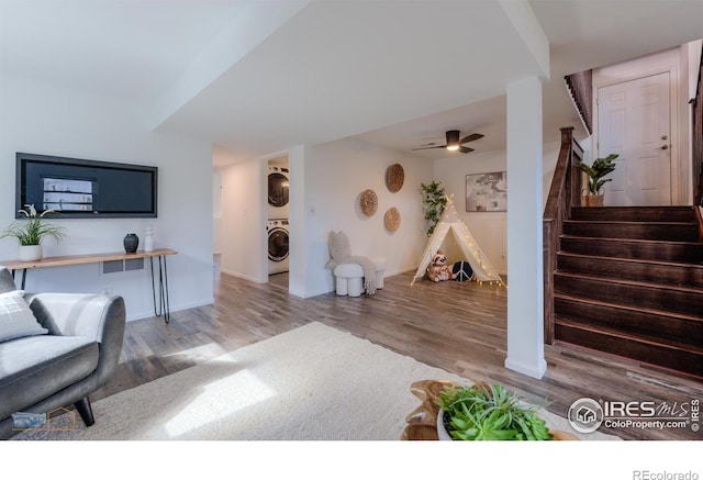 living room with a ceiling fan, stacked washer / dryer, wood finished floors, stairway, and baseboards