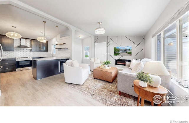 living area with a glass covered fireplace, beverage cooler, and light wood finished floors