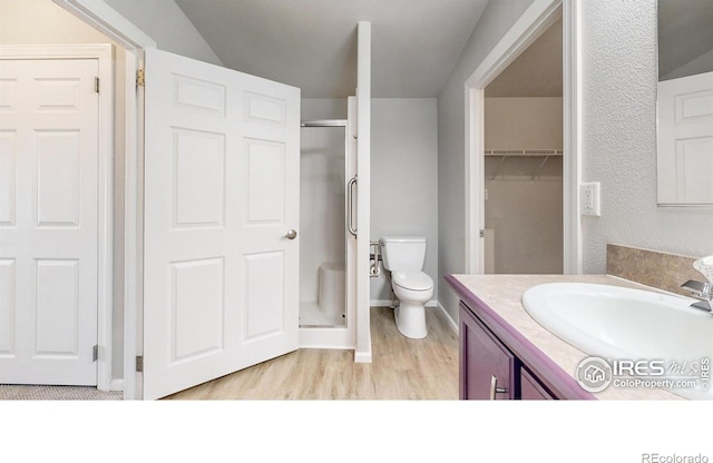 bathroom featuring baseboards, toilet, a stall shower, wood finished floors, and vanity